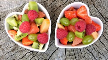 Two heart shaped bowls filled with colorful fruits.