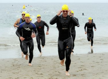 Men in wetsuits running out of the ocean during a race.