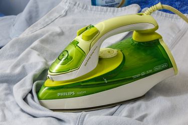 A green Philips iron sitting on a pair of light blue jeans.