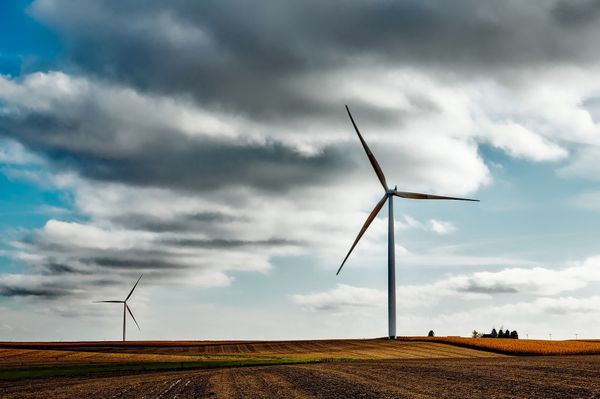 Windmill wind turbines on farmland with clouds above.