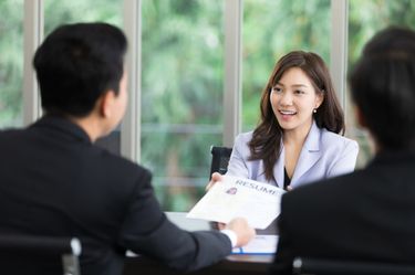 An interviewee handing her résumé to her interviewers during a job interview.