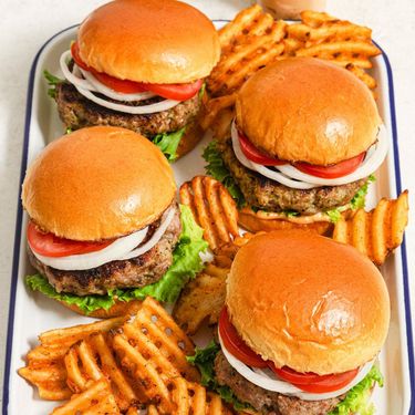 Four hamburgers on a tray with french fries scattered between them.