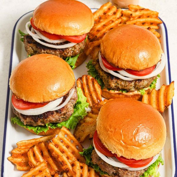 Four hamburgers on a tray with french fries scattered between them.