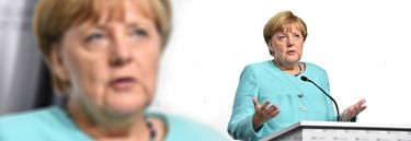 Angela Merkel speaking at a podium in front of a big screen image of her own face.