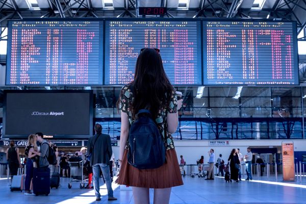 The back of a girl looking up at an electronic flight schedule.