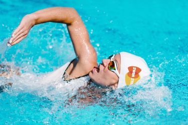 A swimmer wearing a swim cap and goggles takes a breath between strokes.