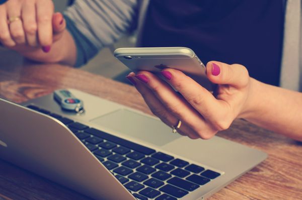 A woman hands are holding an iPhone next to a MacBook.