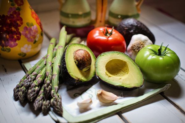 Asparagus, a halved avocado, tomatoes, and garlic on a tray.